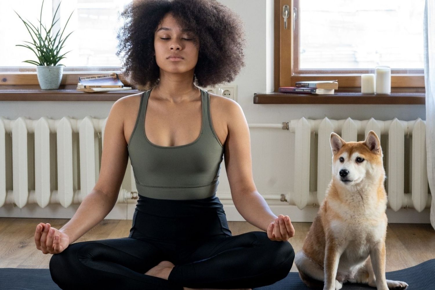 A woman is meditating with a dog in front of her home, addressing dog anxiety.