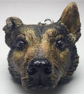 A realistic German shepherd dog head pendant, crafted by a nurse turned sculptor, displayed on a white surface.