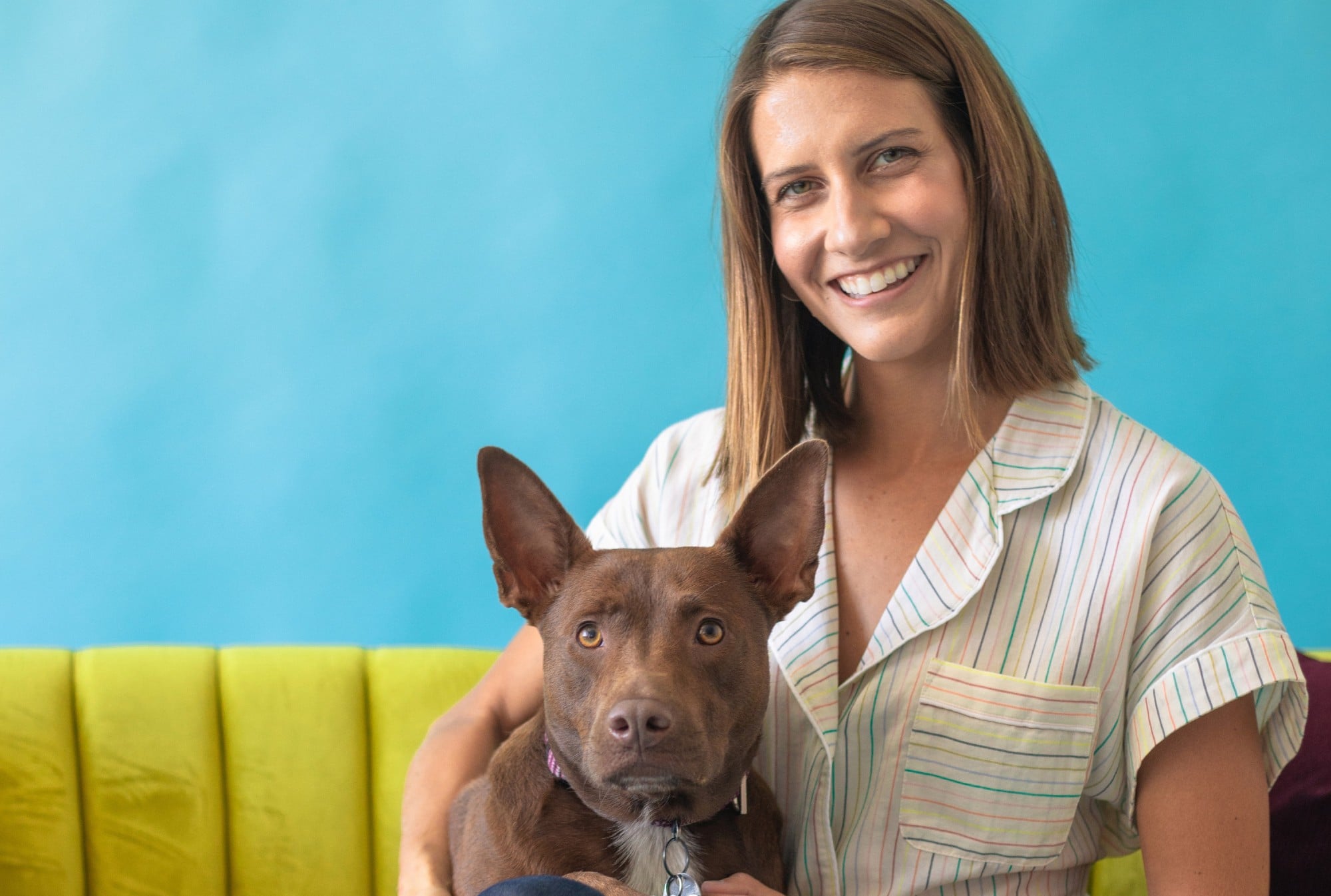 A woman with a brown dog sitting on a couch, teaching the dog words.