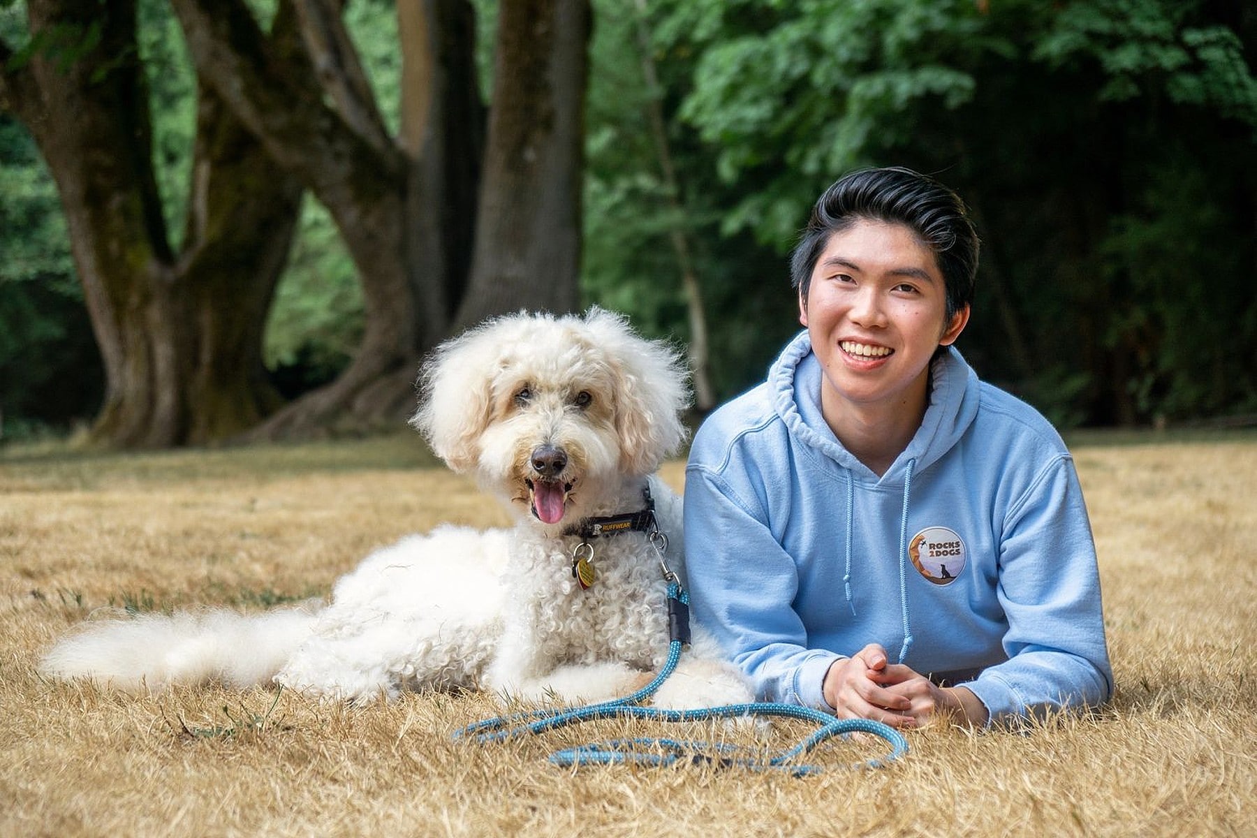 A young man with a shelter dog laying on the grass.