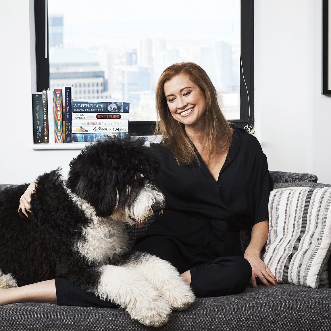 A woman sitting on a couch with a black and white dog, without additional information from the "About Us" description.