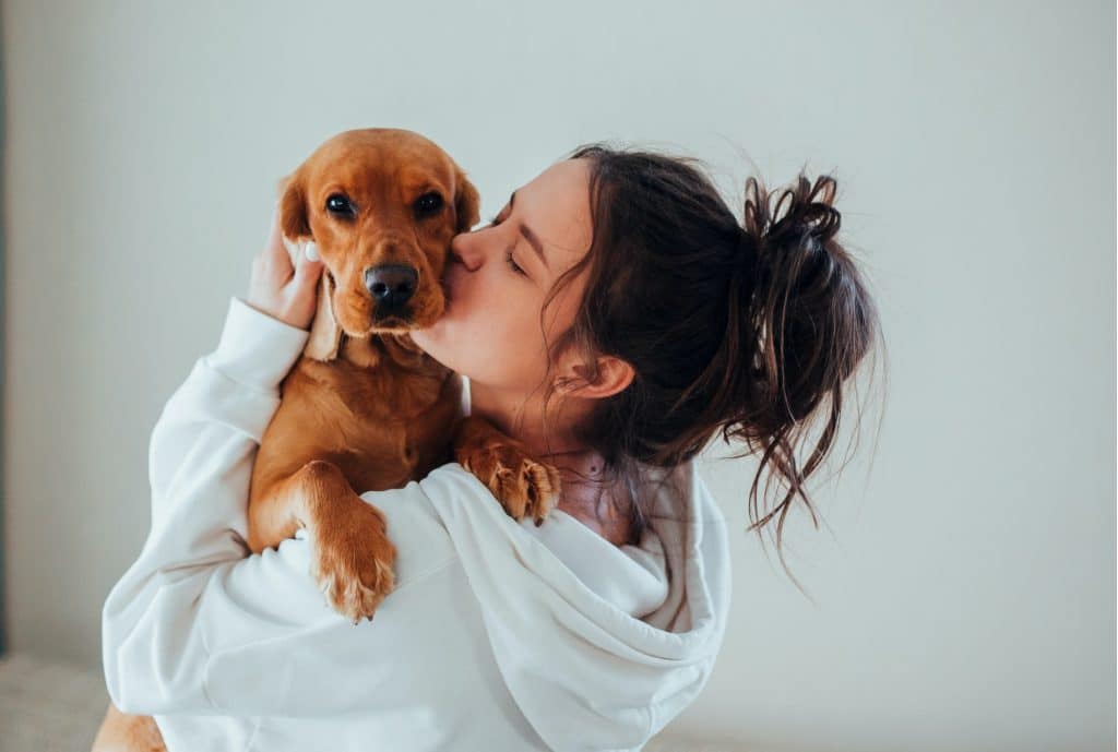 A woman kissing her dog, who has bad breath, in the living room.