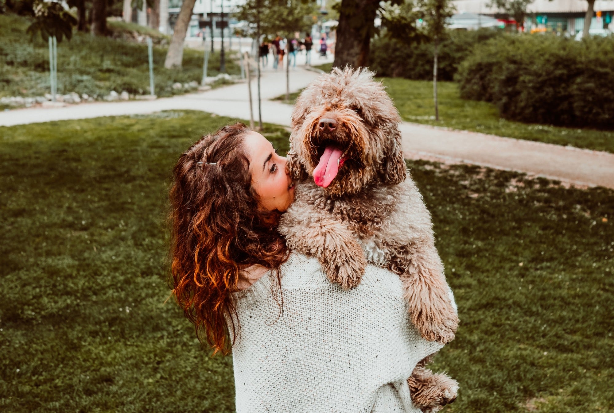 A woman holding her dog in a park, making small changes to their routine to save the environment.